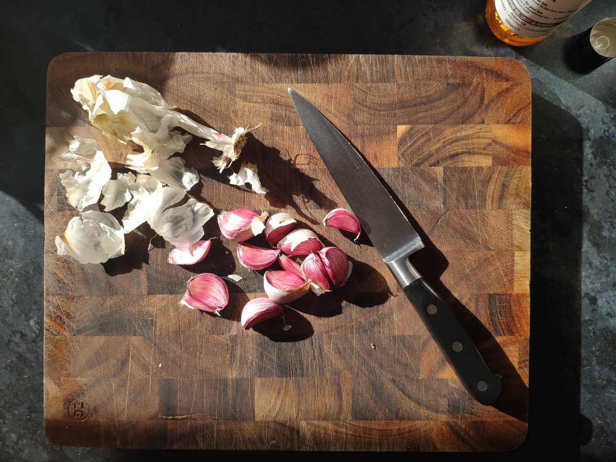 Peeled garlic with knife on wooden board