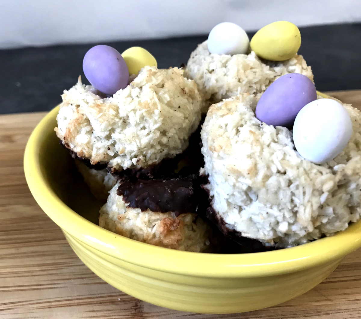 Finished macaroons dipped in dark chocolate with chocolate eggs on top in a yellow bowl