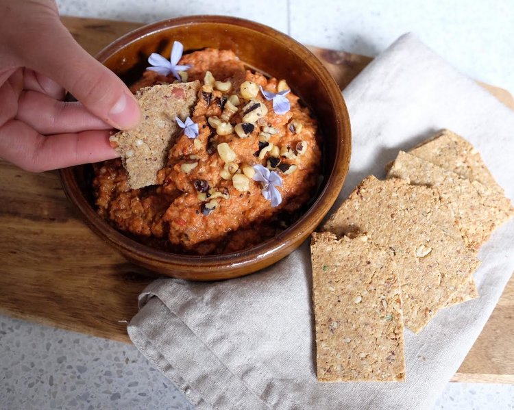 Hand dipping a cracker into roasted red pepper Muhummara Dip